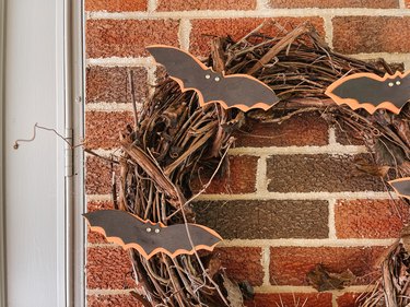 A brick exterior of a house with a grapevine wreath adorned with paper orange and black bats